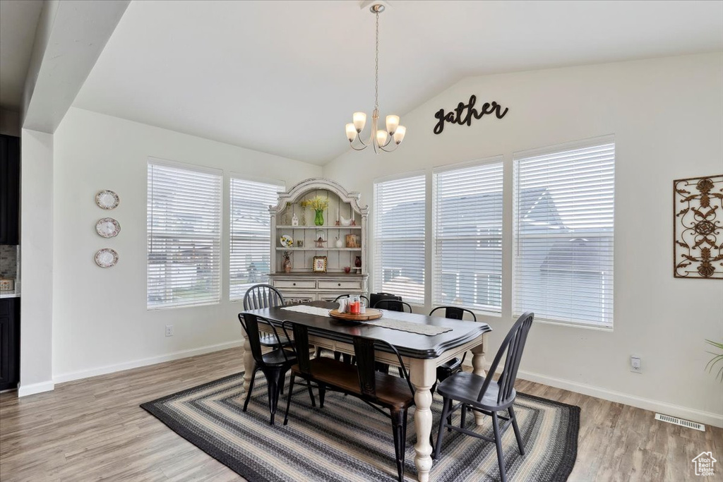 Dining area with a chandelier, vaulted ceiling, light wood-type flooring, and baseboards