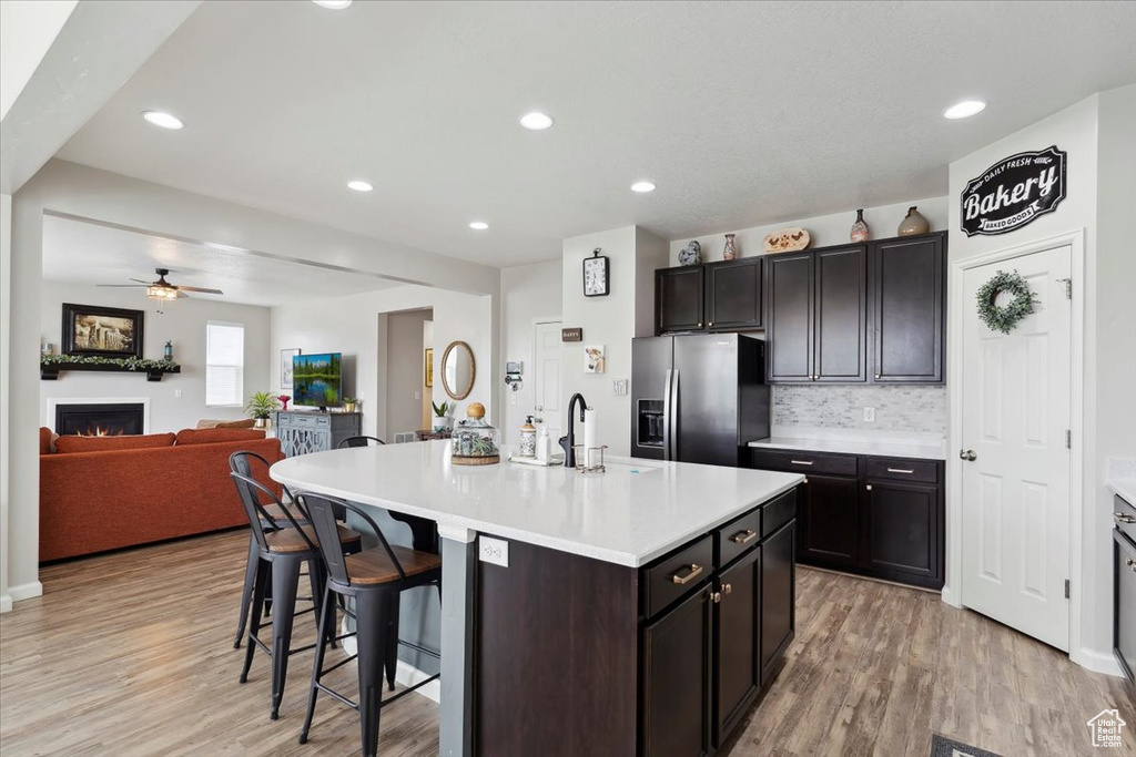 Kitchen with stainless steel refrigerator with ice dispenser, ceiling fan, a kitchen bar, light wood finished floors, and light countertops