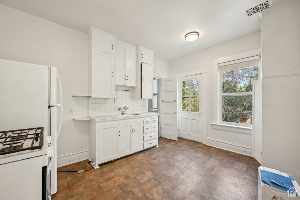 Kitchen featuring light countertops, decorative backsplash, white cabinets, baseboards, and stone finish flooring