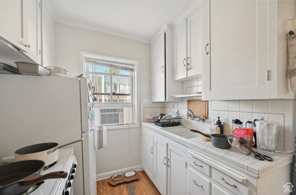 Kitchen featuring white cabinets, tasteful backsplash, light wood-style floors, tile counters, and white appliances