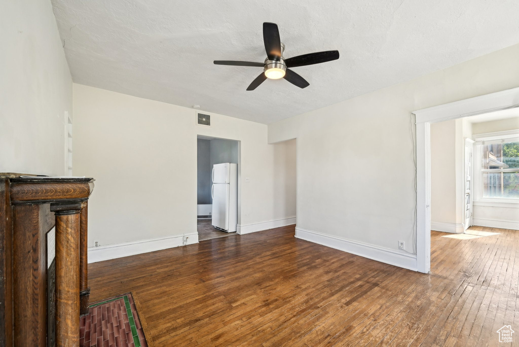 Unfurnished living room featuring a ceiling fan, dark wood-type flooring, and baseboards
