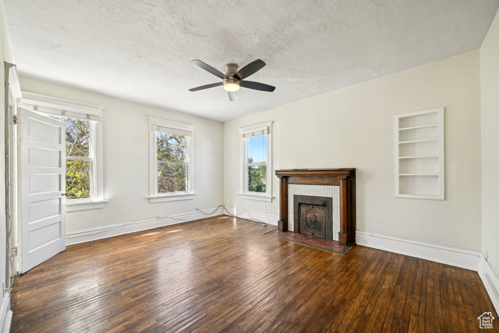 Unfurnished living room featuring a ceiling fan, healthy amount of natural light, wood-type flooring, and a textured ceiling