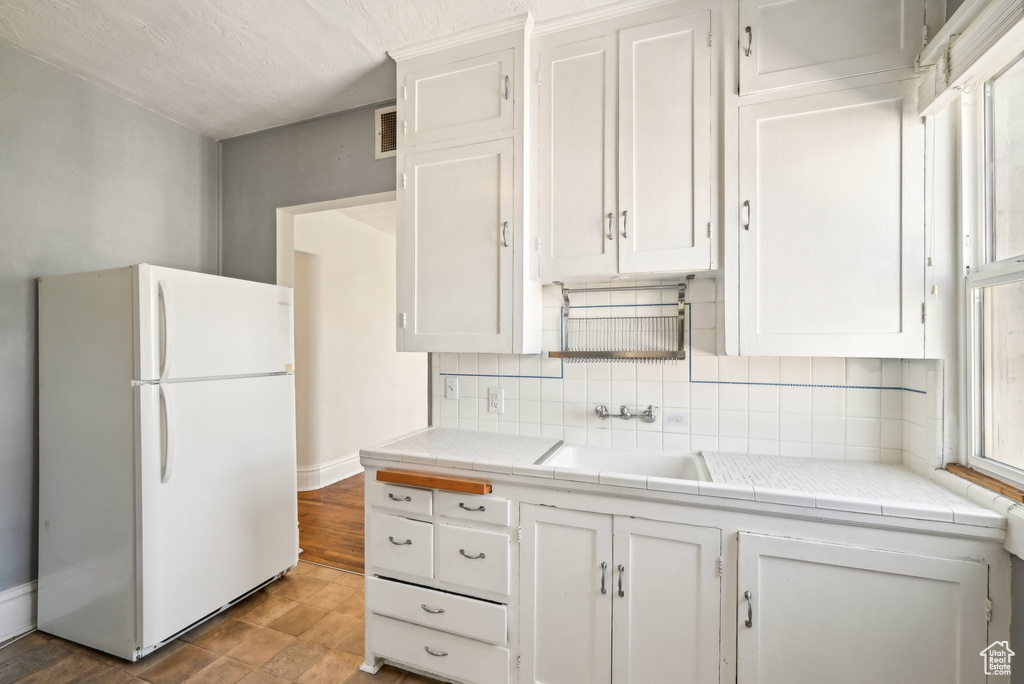 Kitchen with freestanding refrigerator, a sink, tile countertops, and white cabinetry