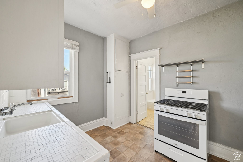 Kitchen featuring gas range gas stove, a sink, ceiling fan, baseboards, and white cabinetry