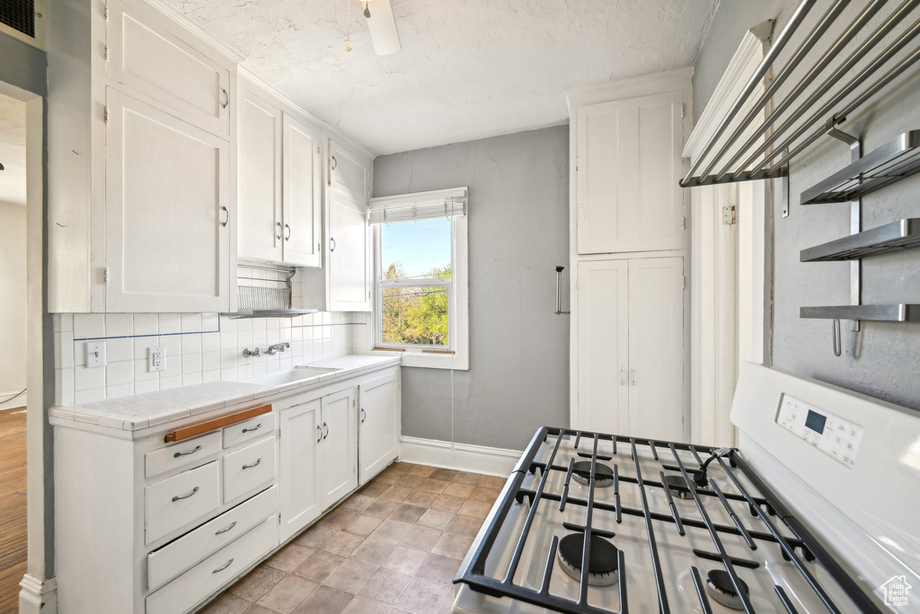 Kitchen with tile counters, open shelves, baseboards, gas range gas stove, and white cabinetry