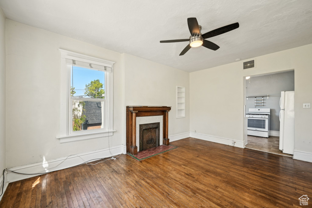 Unfurnished living room with hardwood / wood-style floors, ceiling fan, baseboards, and a brick fireplace