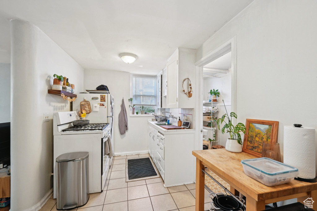 Kitchen with white gas range, white cabinetry, light tile patterned flooring, light countertops, and a sink