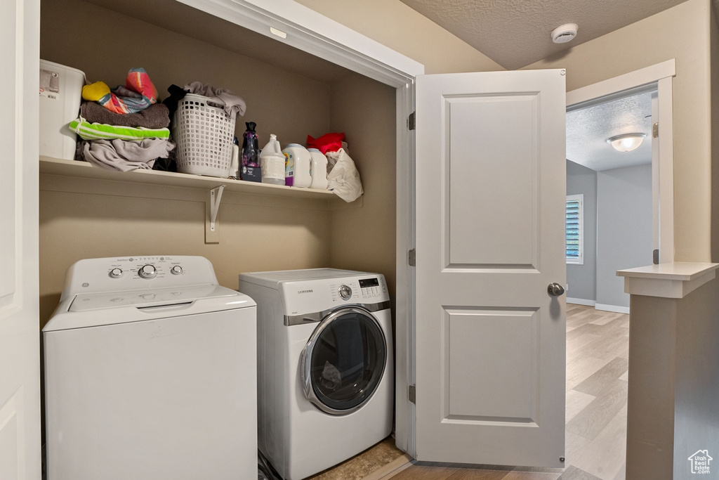 Washroom featuring washing machine and clothes dryer, light wood-style flooring, and a textured ceiling