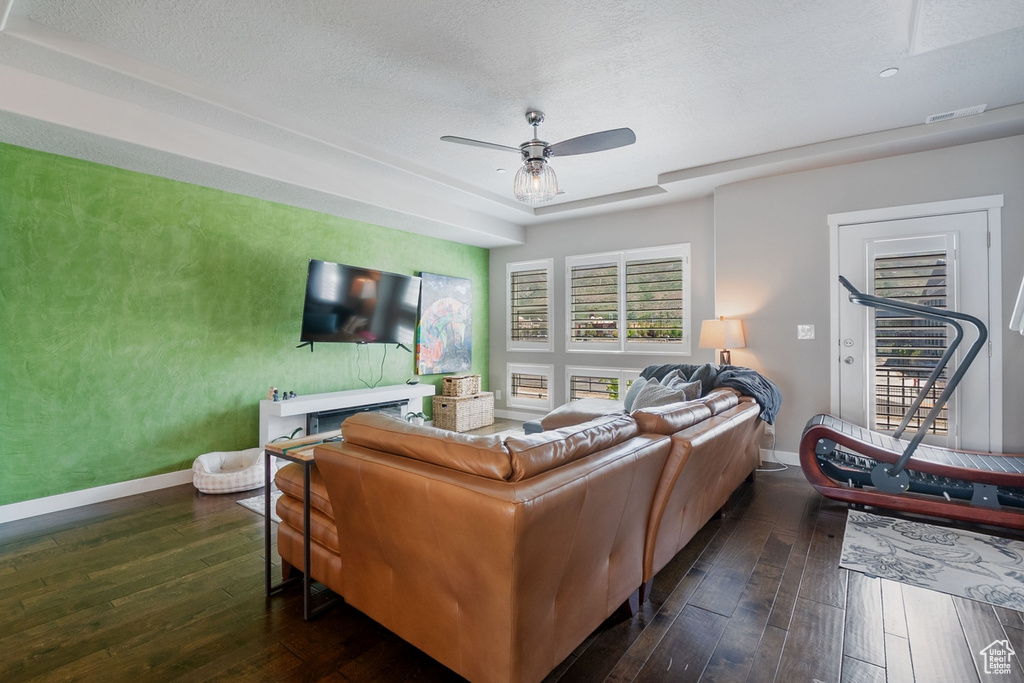 Living room featuring dark wood-type flooring, baseboards, a ceiling fan, and a textured ceiling