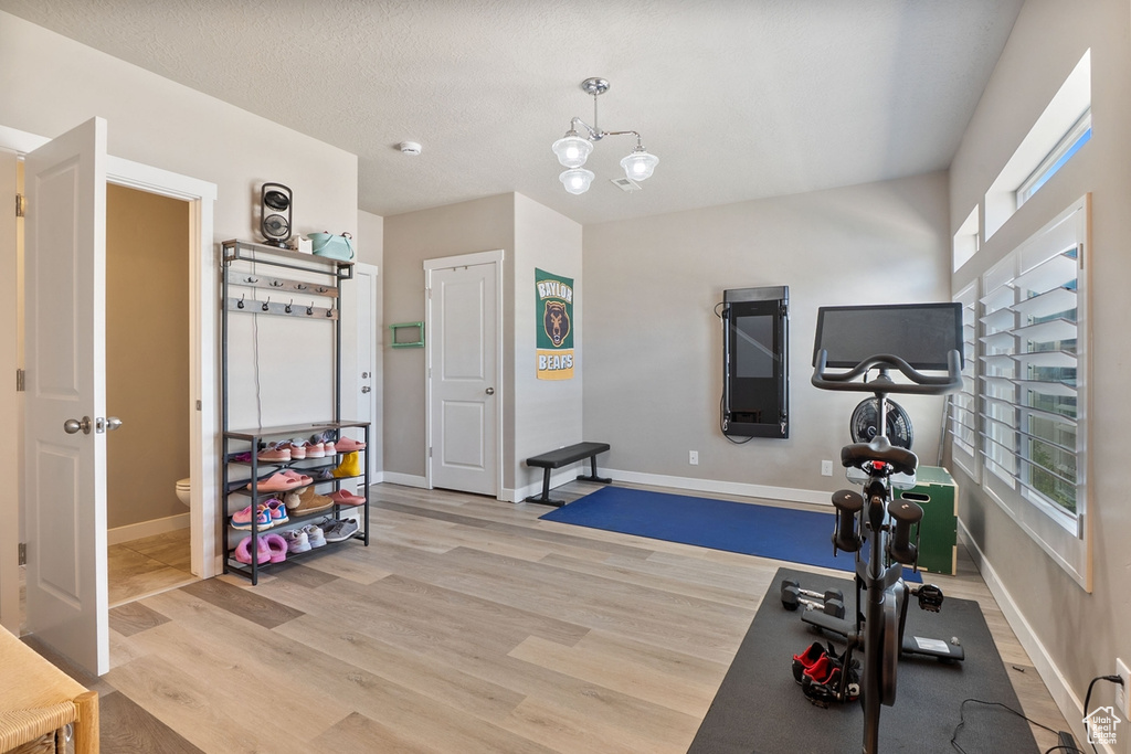 Workout area with light wood-style floors, a chandelier, and baseboards