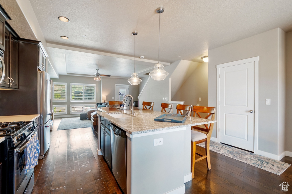 Kitchen with a breakfast bar, appliances with stainless steel finishes, a sink, dark wood-style flooring, and dark brown cabinetry