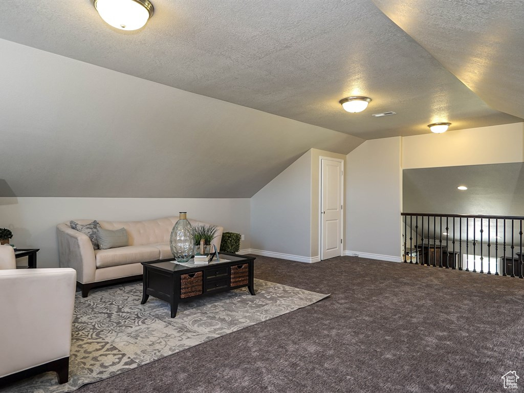 Carpeted living room with vaulted ceiling, a textured ceiling, and baseboards