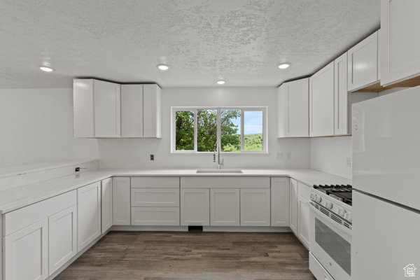 Kitchen with white appliances, a sink, recessed lighting, a textured ceiling, and white cabinetry