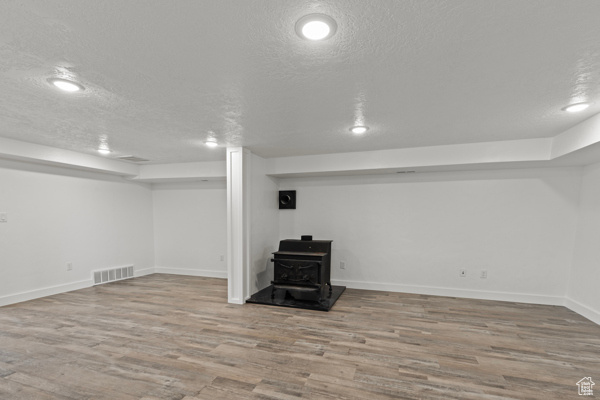 Finished below grade area with a wood stove, a textured ceiling, wood finished floors, and baseboards