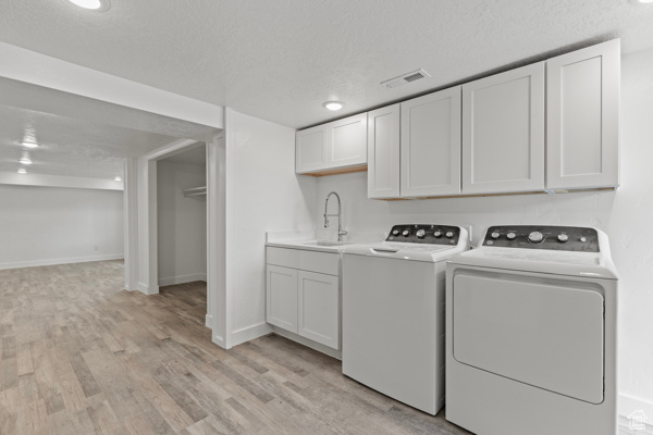 Clothes washing area with a sink, washer and clothes dryer, light wood-style flooring, a textured ceiling, and baseboards