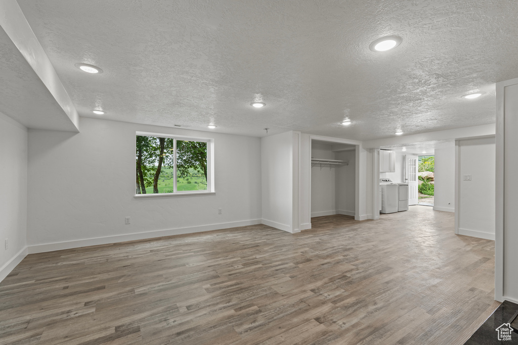 Unfurnished living room featuring washing machine and clothes dryer, light wood-type flooring, a textured ceiling, baseboards, and recessed lighting