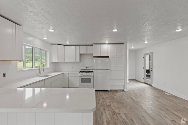 Kitchen featuring white appliances, a sink, a peninsula, light stone counters, and light wood-style flooring