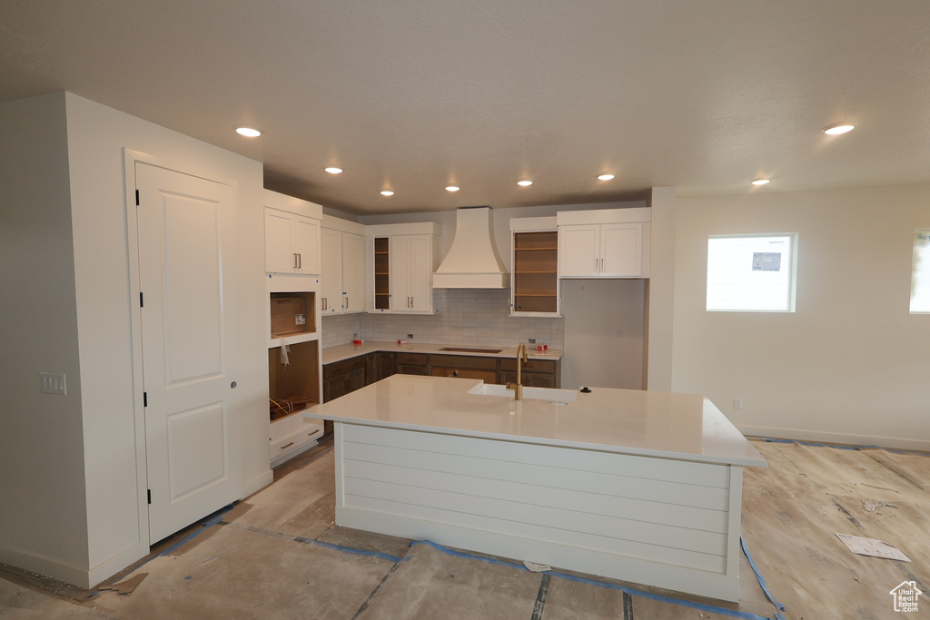 Kitchen with premium range hood, a center island with sink, black electric cooktop, decorative backsplash, and white cabinets