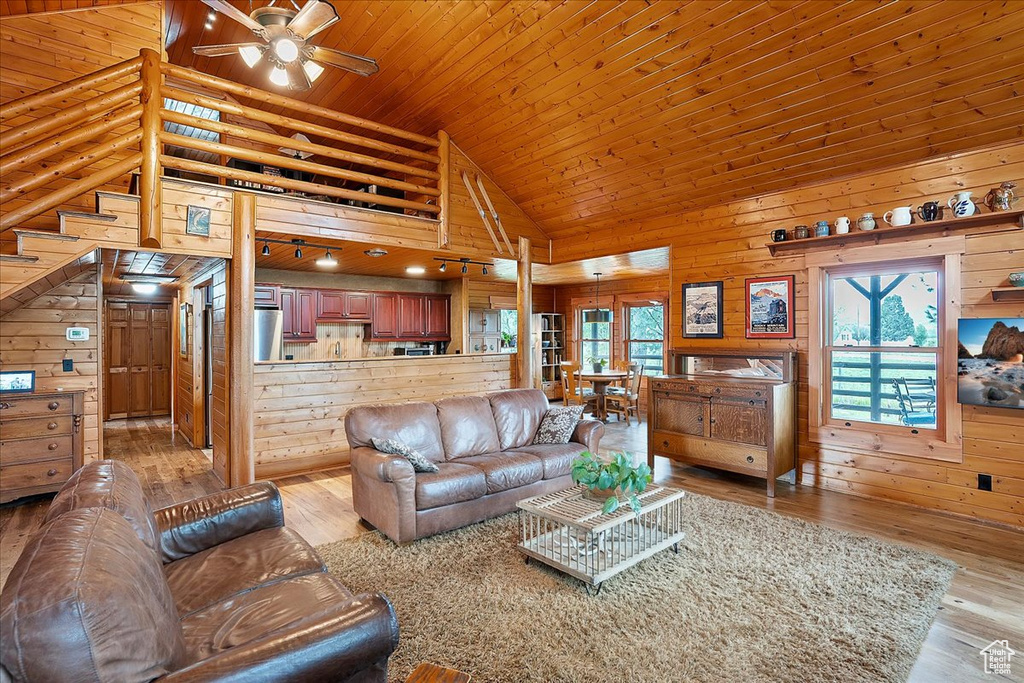 Living room featuring healthy amount of natural light, light wood finished floors, a ceiling fan, high vaulted ceiling, and wooden walls