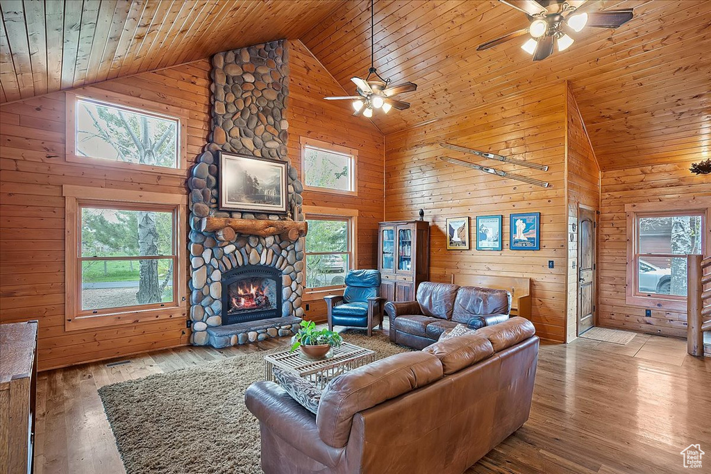 Living area with a ceiling fan, high vaulted ceiling, wood walls, wood ceiling, and a fireplace
