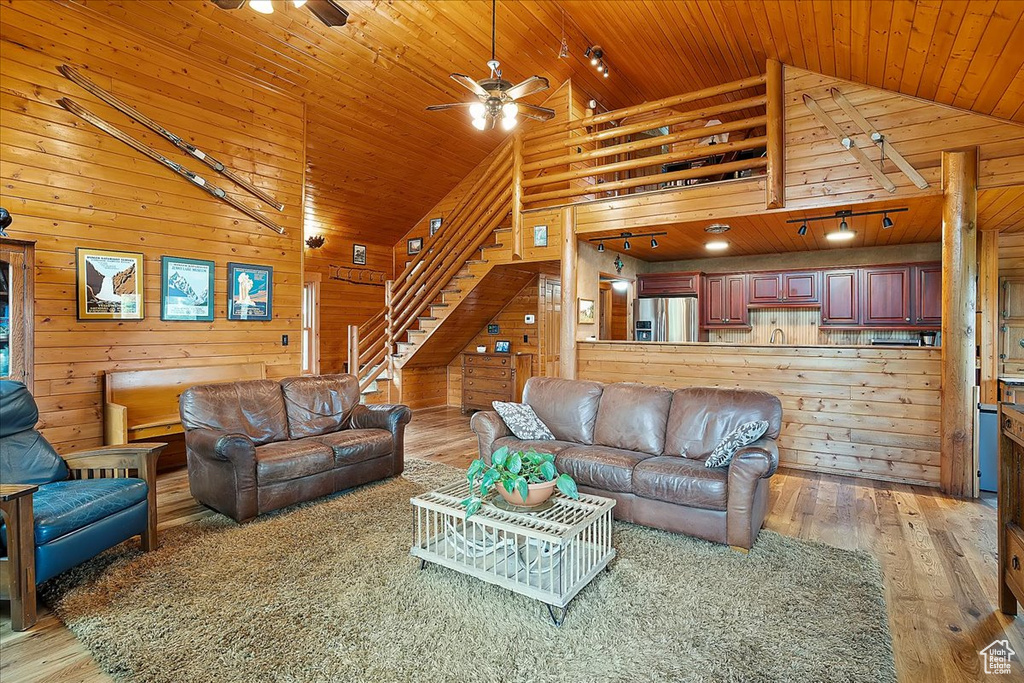 Living room with a ceiling fan, light wood-style floors, vaulted ceiling, wooden ceiling, and wood walls