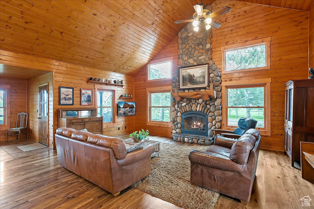 Living area featuring high vaulted ceiling, wood walls, ceiling fan, a fireplace, and light wood-style flooring