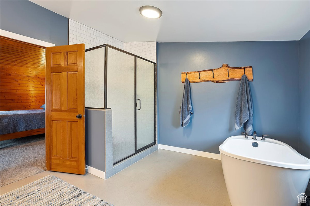 Full bathroom with a stall shower, a freestanding bath, baseboards, and finished concrete flooring