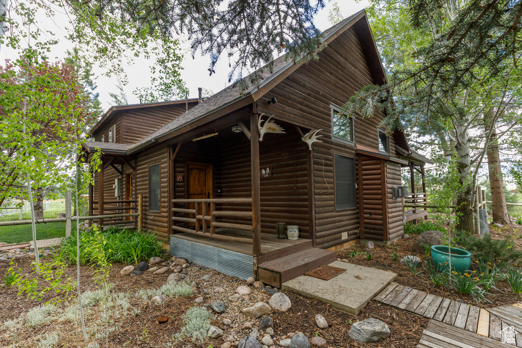 View of front facade with log veneer siding, a porch, and a shingled roof