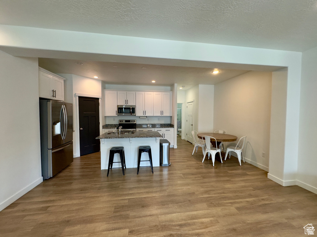 Kitchen featuring stainless steel appliances, white cabinetry, a kitchen breakfast bar, an island with sink, and baseboards
