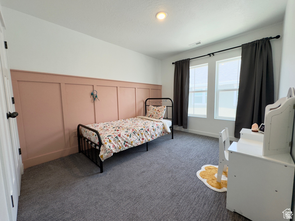 Bedroom featuring a decorative wall, carpet floors, and a wainscoted wall