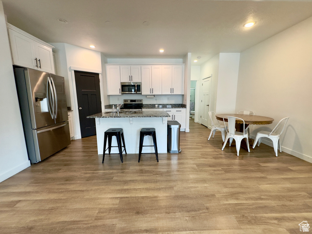 Kitchen with appliances with stainless steel finishes, white cabinets, light wood-style flooring, a kitchen breakfast bar, and a kitchen island with sink