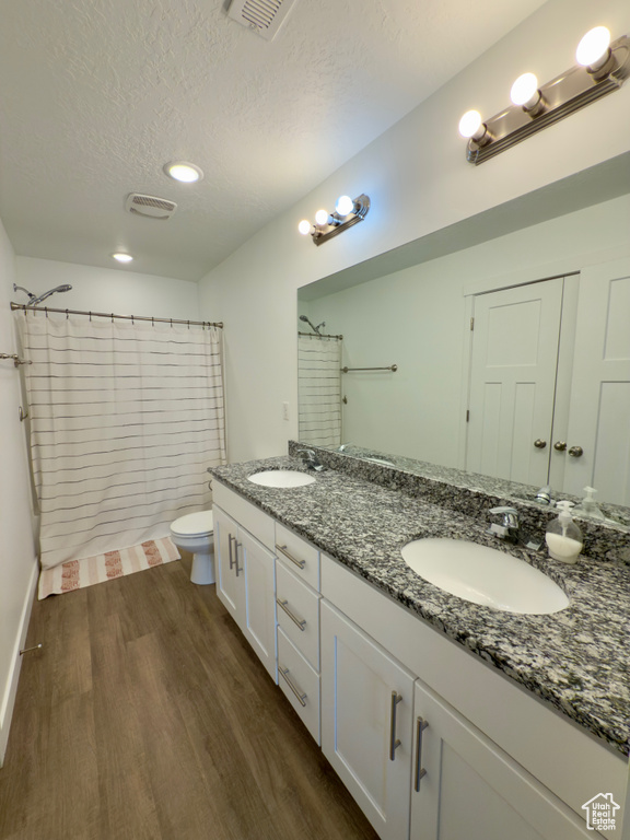 Full bath featuring wood finished floors, a textured ceiling, toilet, double vanity, and a shower with shower curtain