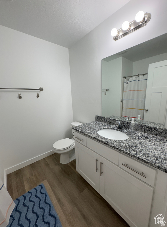 Full bath with wood finished floors, vanity, toilet, baseboards, and a textured ceiling