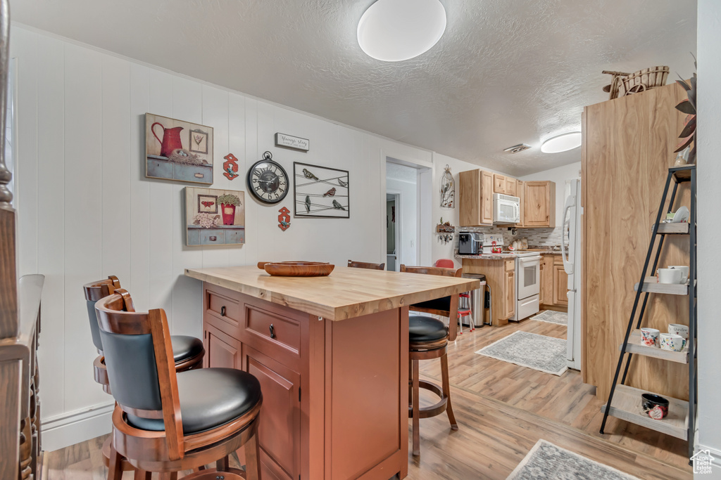 Kitchen featuring white appliances, butcher block counters, a kitchen breakfast bar, light wood-style flooring, and a textured ceiling