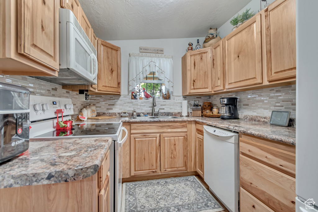 Kitchen with white appliances, a sink, light brown cabinets, tasteful backsplash, and light countertops