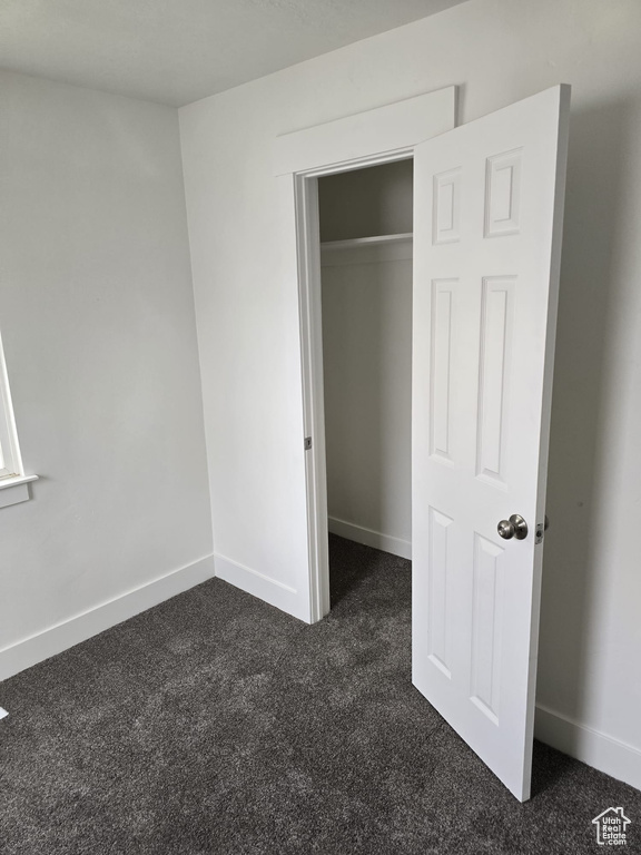 Unfurnished bedroom with dark carpet, baseboards, and a closet