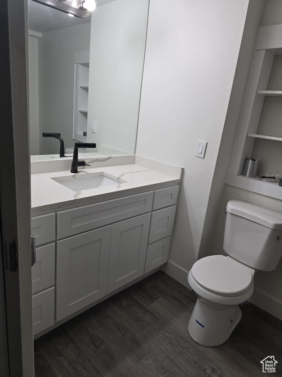 Half bath featuring wood finished floors, toilet, vanity, and baseboards