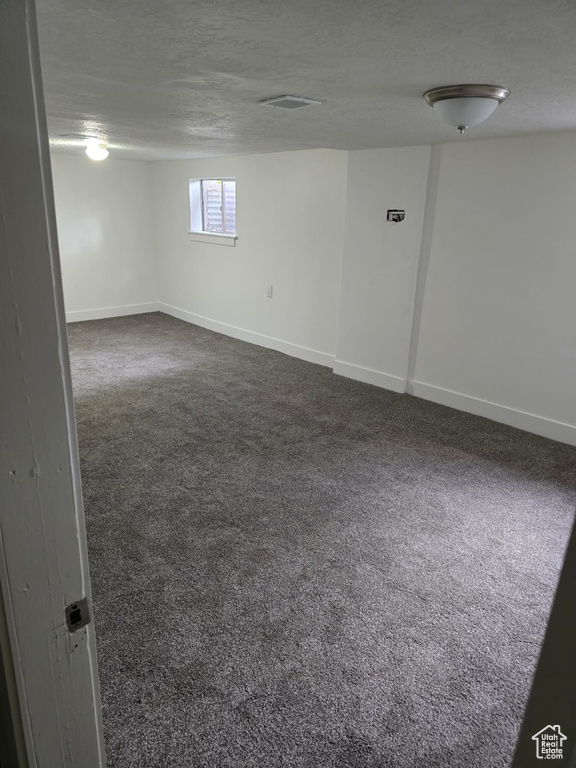 Below grade area featuring dark carpet, baseboards, and a textured ceiling