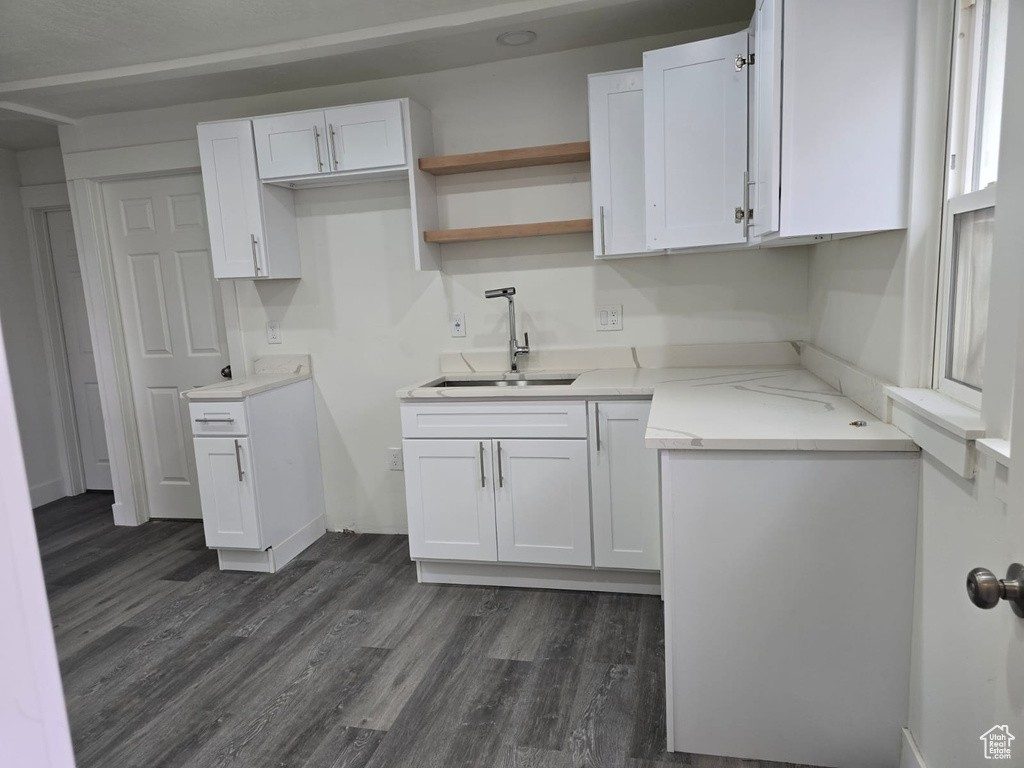 Kitchen with a sink, white cabinetry, dark wood-style floors, light countertops, and baseboards