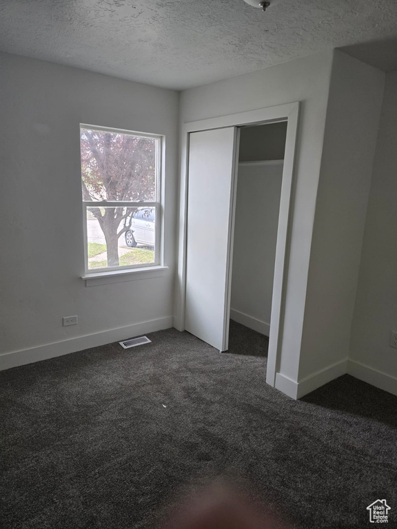 Unfurnished bedroom featuring dark carpet, baseboards, a textured ceiling, and a closet