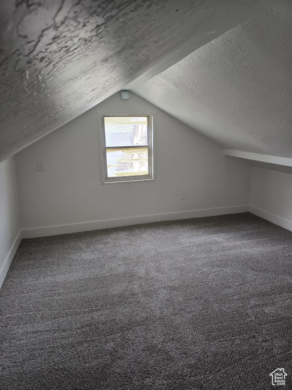 Bonus room with a textured ceiling, lofted ceiling, baseboards, and carpet flooring