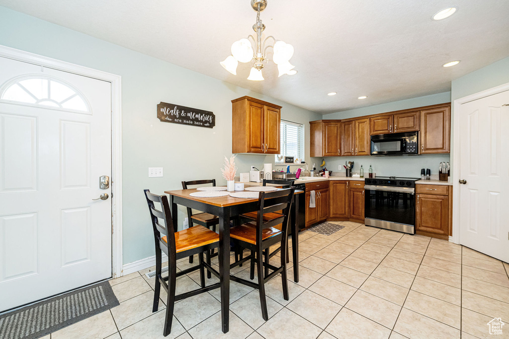 Kitchen featuring stainless steel range with electric stovetop, black microwave, a chandelier, light tile patterned floors, and brown cabinetry