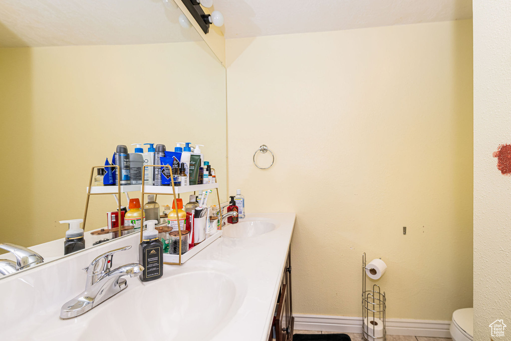 Bathroom featuring double vanity, toilet, and baseboards