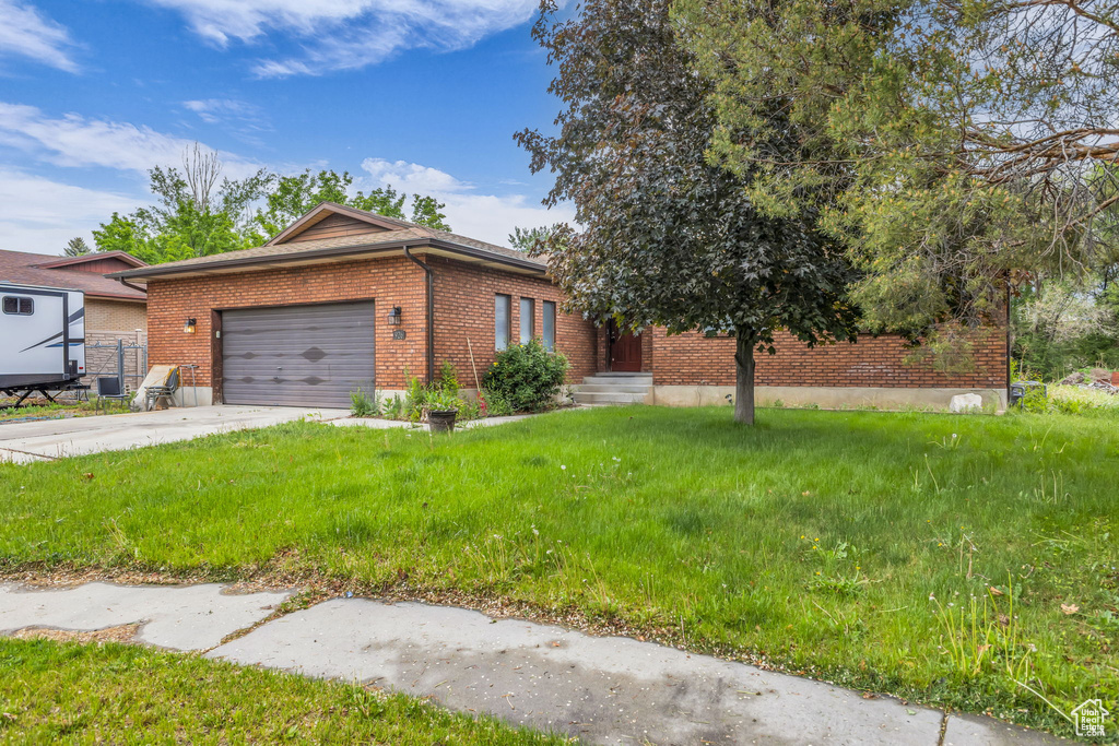 View of front of house featuring brick siding, a garage, driveway, and a front lawn