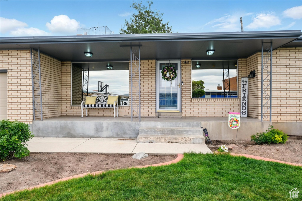 View of exterior entry featuring covered porch and brick siding