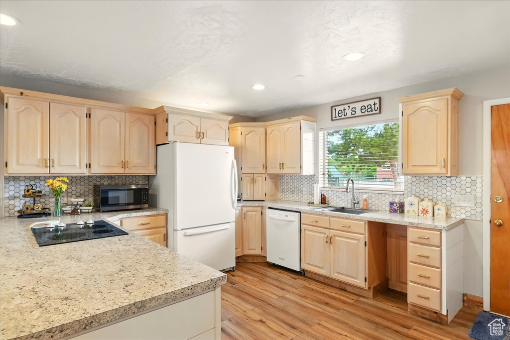 Kitchen featuring white appliances, light brown cabinetry, a sink, decorative backsplash, and recessed lighting