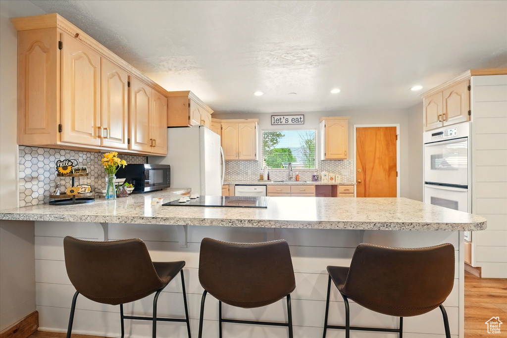 Kitchen featuring a peninsula, black appliances, light brown cabinets, a sink, and recessed lighting