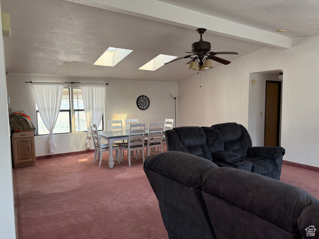Carpeted living room featuring a skylight, baseboards, ceiling fan, and a textured ceiling