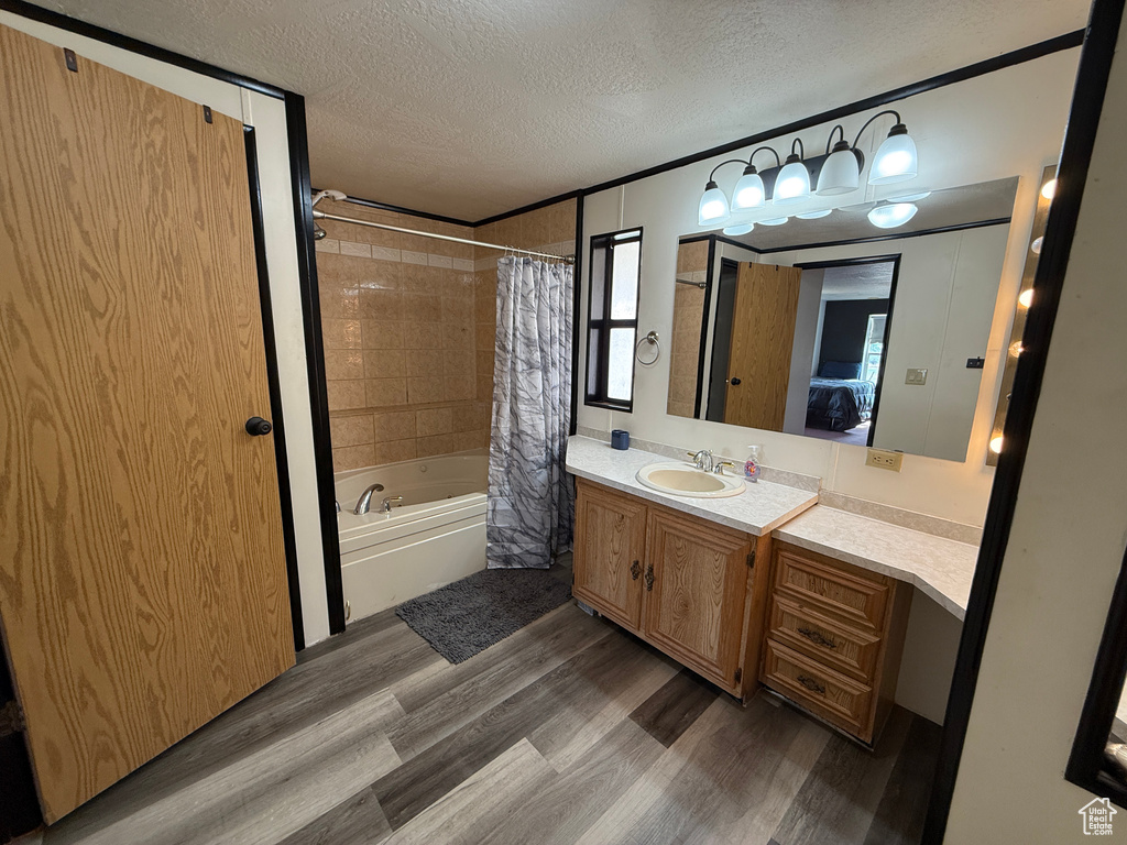Ensuite bathroom featuring a textured ceiling, wood finished floors, shower / bath combo with shower curtain, and vanity