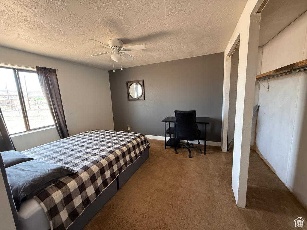 Carpeted bedroom with a textured ceiling, a ceiling fan, and a desk